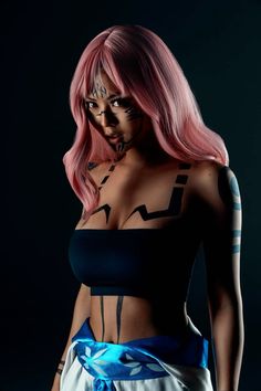 a woman with pink hair and tattoos on her chest posing for a photo in front of a dark background