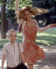 a woman in an orange dress is standing next to a young boy with her arms outstretched