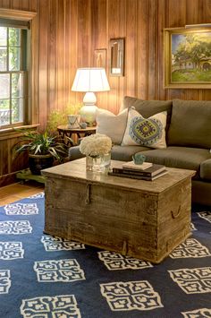 a living room with wood paneling and blue carpeted flooring, two lamps on either side of the coffee table