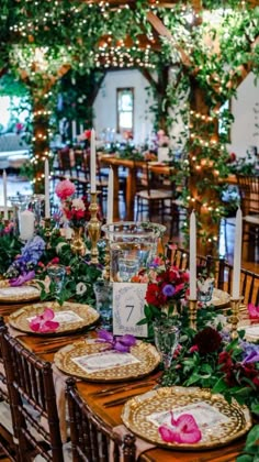 the table is set with place settings and flowers on it, along with candles and greenery