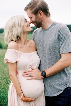 a pregnant couple cuddles in the middle of a field