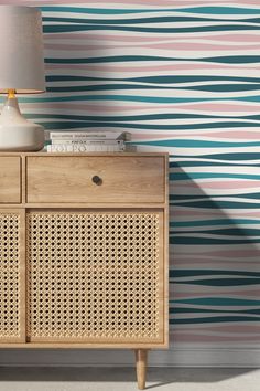 a wooden cabinet sitting next to a wall with a lamp on top of it in front of a blue and pink striped wallpaper