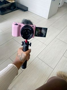 a person holding a camera with a microphone attached to it's tripod in front of a tile floor