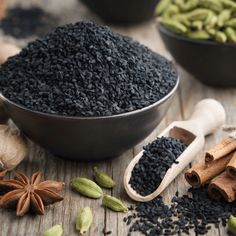 an assortment of spices and herbs on a wooden table next to bowls of black seed