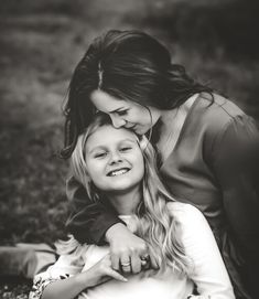 mother and daughter cuddling on the ground in black and white photo with grass behind them