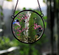 a bird sitting on top of a green plant in a glass bowl hanging from a chain