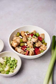 two bowls filled with food sitting on top of a table next to celery