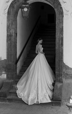 black and white photo of woman in wedding dress standing on stairs with light fixture above her head