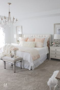 a bedroom with a white bed, chandelier and two tables in front of it