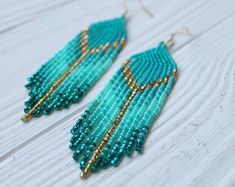 turquoise beaded earrings with gold accents on white wooden background, closeup view from the bottom