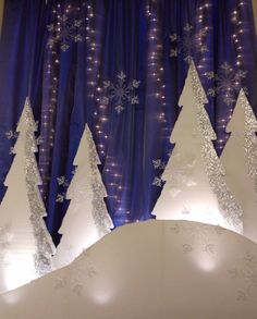 lighted christmas trees on display in front of a blue curtain with snowflakes and lights