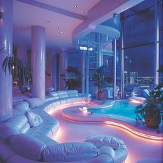 a living room filled with lots of white furniture next to a swimming pool at night