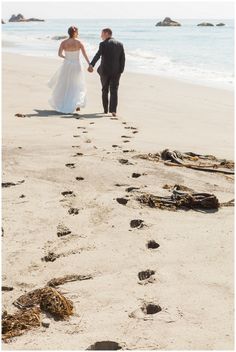 a bride and groom walking on the beach with footprints in the sand near the water