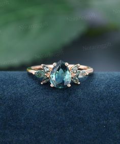 an aqua ring with three pear shaped stones on it's side, sitting on top of a blue cloth