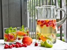 a pitcher filled with water next to two glasses full of liquid and fruit on the table