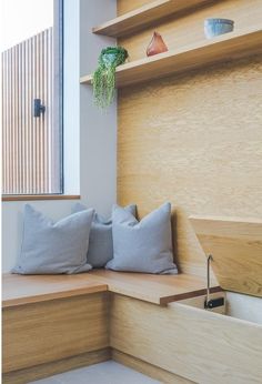 two pillows sit on the bench in front of a window with wooden shelves and planters