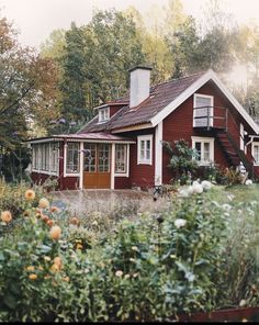 a red house in the woods with flowers around it