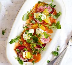 a white plate topped with lots of veggies next to a fork and knife