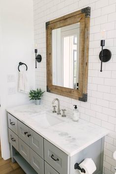 a bathroom with white and gray cabinets, a wooden mirror over the sink and a wood framed mirror on the wall