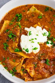 a white bowl filled with tortellini soup topped with sour cream and parsley