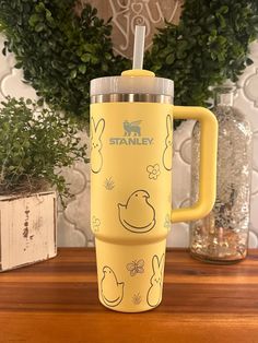 a yellow travel mug sitting on top of a wooden table next to a potted plant