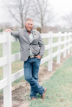 a man leaning against a white fence posing for the camera