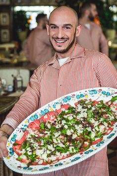 a man holding a large pizza with lots of toppings on it's platter