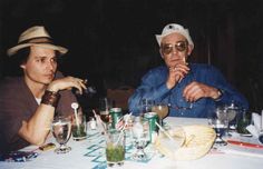 two people sitting at a table with glasses and drinks in front of them, one wearing a cowboy hat