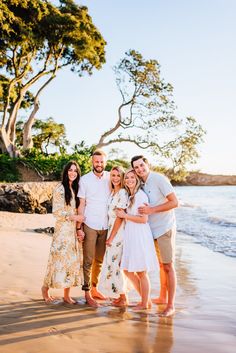 a group of people standing on top of a sandy beach next to the ocean with trees in the background