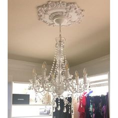 a chandelier hanging from the ceiling in a room with clothes on hangers