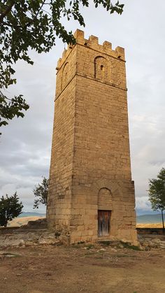 an old brick tower with a door in the middle and trees around it on a cloudy day