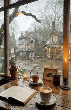 a cup of coffee sitting on top of a wooden table next to a book and candle