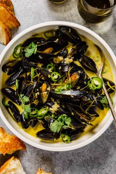 a white bowl filled with mussels and greens next to some bread on a table