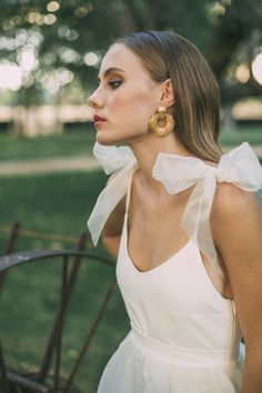 a woman in a white dress with large gold hoop earrings on her neck and shoulders