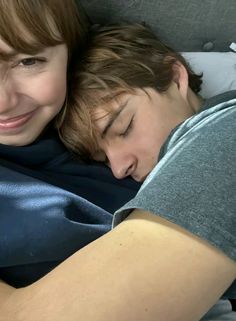 two people laying in bed with their arms around each other and smiling at the camera