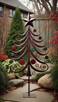 a metal christmas tree with red balls and stars on it's top, sitting in the middle of a garden