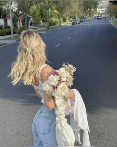 a woman is walking down the street with flowers in her hair and holding a bouquet