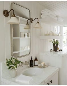 a white sink sitting under a mirror next to a vase with pink flowers in it