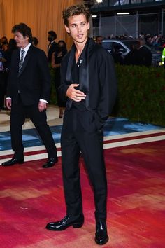 a man in a black suit and tie standing on a red carpet with other people