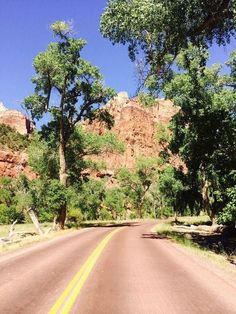 an empty road with trees and mountains in the background on a sunny day at red rock canyon state park