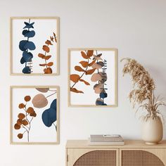 three framed art pieces hang on the wall above a wooden cabinet with a plant in it