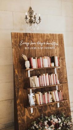 a wooden book shelf with books on it next to a chandelier and flowers