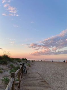 a bike parked on top of a wooden ramp next to the beach at sunset with people in the background