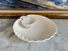 a large white shell shaped bowl sitting on top of a marble floor next to a painting