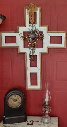 a cross is hanging on the wall next to an old clock and vase with flowers