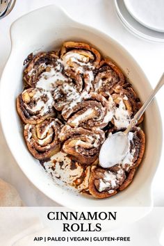 cinnamon rolls with icing in a white bowl on a table next to silverware