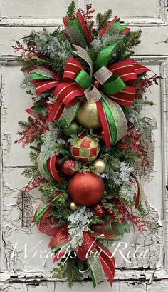 a christmas wreath hanging on the side of a door with ornaments and ribbons around it