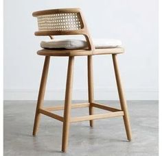 a wooden stool with a woven seat and backrest on concrete flooring, in front of a white wall