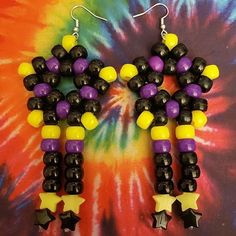 a pair of black, yellow and purple beaded earrings on a tie dye background