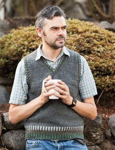 a man standing in front of some rocks holding a cup